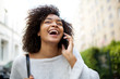 © mimagephotos - Close up happy young african american woman with curly hair talking with mobile phone outside