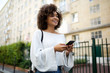 © mimagephotos - smiling young african american woman walking in city with mobile phone in hand