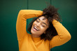 © mimagephotos - Close up cheerful young african american woman laughing with hand in hair by green background