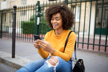Smiling African American Young Woman Looking At Cellphone In City