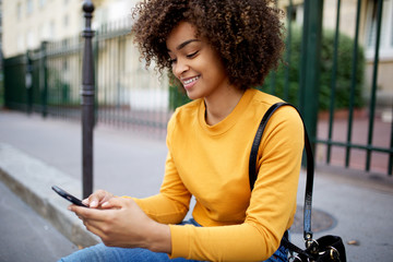 Wall Mural - smiling african american woman looking at cellphone in city