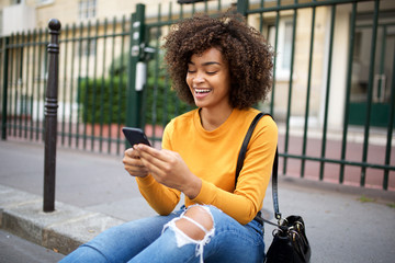 Wall Mural - smiling african american young woman looking at cellphone in city