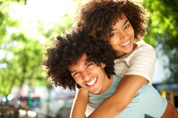 Wall Mural - close up happy afro man giving piggyback to smiling girlfriend outside