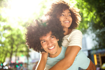 Close up smiling afro man giving piggyback to happy girlfriend outside