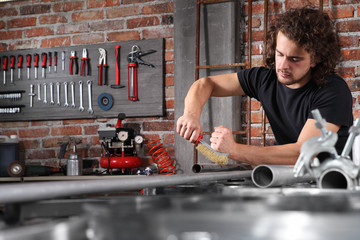 man in home workshop garage work metal with handle wire brush, repair, brushes and cleaning iron pipe on the workbench full of wrenches, diy and craft concept