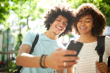 Wall Mural - happy young african american couple standing outside looking at cellphone