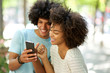 © mimagephotos - happy afro man showing smiling african american young woman mobile phone