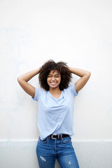 Wall Mural - happy young african american woman laughing with hands behind head by white wall