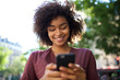 © mimagephotos - Close up smiling young african american woman looking at cellphone outdoors