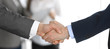 © rogerphoto - Business people shaking hands while standing with colleagues after meeting or negotiation, close-up. Group of unknown businessmen and women in modern office. Teamwork, partnership and handshake