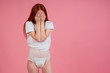 young amazed and surprised redhaired ginger woman wearing incontinence diaper in studio pink background.feeling shame and embarrassment