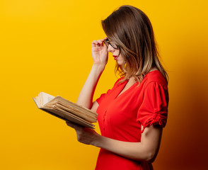 Wall Mural - Beautiful woman in red dress with book on yellow background