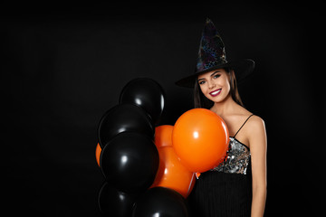 Wall Mural - Beautiful woman wearing witch costume with balloons for Halloween party on black background