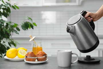 Poster - Woman pouring water from modern electric kettle into cup at grey table in kitchen, closeup