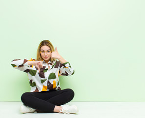 Wall Mural - young blonde woman feeling confused, clueless and unsure, weighting the good and bad in different options or choices sitting on the floor