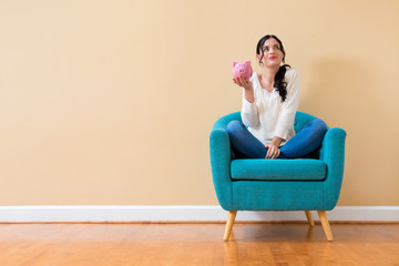 Wall Mural - Young woman with a piggy bank sitting in a chair