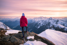 Young Woman In Snowy Mountains At Sunset In Winter. Beautiful Slim Girl On The Mountain Peak Against Snow Covered Rocks And Colorful Red Sky With Clouds In The Evening. Travel In Dolomites. Tourism