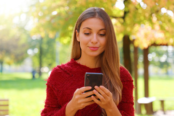 Wall Mural - Close up of beautiful girl using internet browsing on smart phone on Autumn or Winter season.