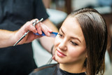Fototapeta Na ścianę - Hairdresser is making hairstyle for young woman with wet brown long hair at hair salon close up.