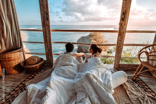 Fotografía Couple enjoying morning vacations on tropical beach bungalow looking ocean view
