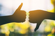 Silhouette image of two hands making thumbs up and thumbs down sign