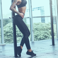 Wall Mural - legs of young slim athletic woman in sportswear posing in gym, image with cold vintage toning