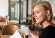 Young blonde woman having a breakfast with coffee reading newspaper in cafe.