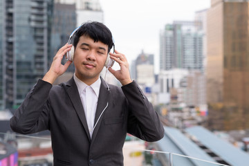 Wall Mural - Young Asian businessman listening to music against view of the city