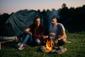 Wall Mural - romantic couple on camping by the camping fire barbecuing sausages