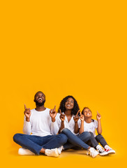 Wall Mural - Afro family of three sitting on floor and pointing upwards