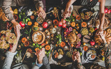 Fototapeta Na ścianę - Family praying holding hands at Thanksgiving table. Flat-lay of feasting peoples hands over Friendsgiving table with Autumn food, candles, roasted turkey and pumpkin pie over wooden table, top view