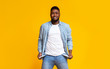 Desperate african american guy showing empty pockets over yellow background