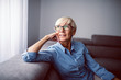 © dusanpetkovic1 - Portrait of thoughtful smiling caucasian senior woman sitting on sofa in living room and looking trough window.