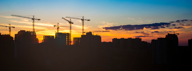 construction in the rays of sunset. tower cranes silhouettes over amazing sunset sky