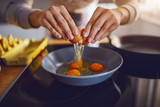 Close up of caucasian woman breaking egg and making sunny side up eggs. Domestic kitchen interior. Breakfast preparation.