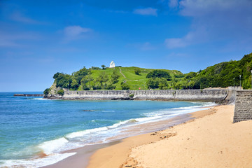 Landscape with a sandy beach and embankment of Saint-Jean-de-Luz, green hill with white chapel on top (Basque Country, Atlantic coast, France). Coastal french town at sunny summer day. Sea shore