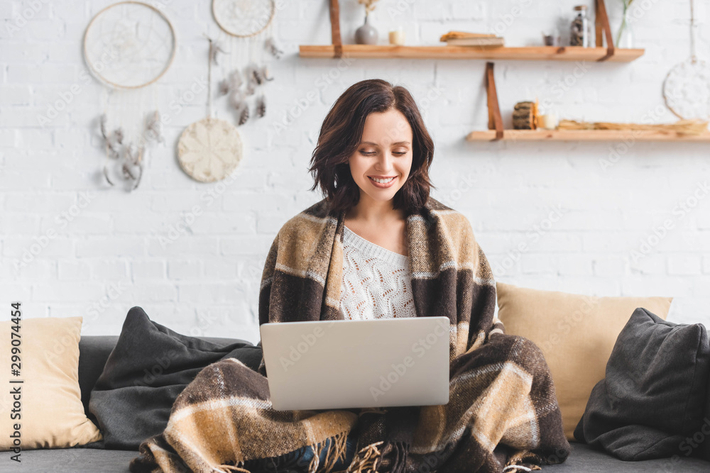 beautiful cheerful girl in blanket using laptop in living room with dream catchers - obrazy, fototapety, plakaty 