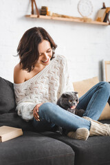 Wall Mural - happy young woman sitting on sofa with scottish fold cat