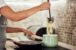 © nenadaksic - Cropped picture of mixed race woman in apron standing next to stove and making spaghetti.