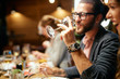 © chika_milan - Handsome caucasian bearded hipster man with eyeglasses drinking wine while sitting with his friends in restaurant.