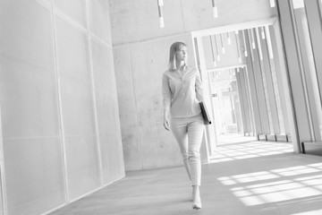 Wall Mural - Black and white photo of businesswoman walking while holding document in office hall