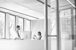 © MDBPIXS - Black and white photo of businessman sitting on table while talking to receptionist in office lobby during break