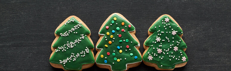 flat lay with delicious glazed Christmas tree cookies on black wooden table, panoramic shot