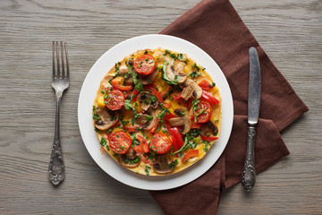 homemade omelet with vegetables on wooden table with fork, knife and napkin