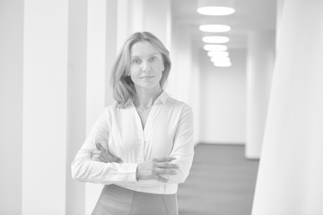 Wall Mural - Black and white photo of confident businesswoman standing with arms crossed in corridor at office