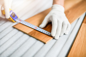 Wall Mural - Close up of wood worker with in white gloves measuring tape and new laminated wooden floor board.