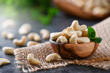 Wall Mural - Cashew nuts in wooden bowl on dark black table with mint leaf on top. Raw cashews side view.