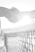 Midsection Of Men Shaking Hands While Standing At Tennis Court Against Clear Sky