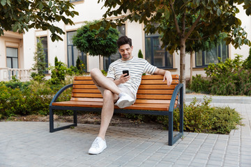 Wall Mural - Image of happy young man using smartphone and smiling while sitting