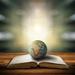 Wall Mural - An old globe lying on an open book against the background of library. Selective focus. Retro style. Science, education, travel, vintage background. Education history and geography team.